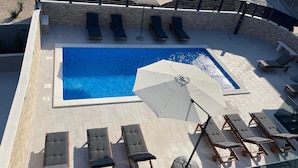 A rooftop pool with multiple sun loungers and a large umbrella. - Apartments Villa Milas With Pool (Jesenice)