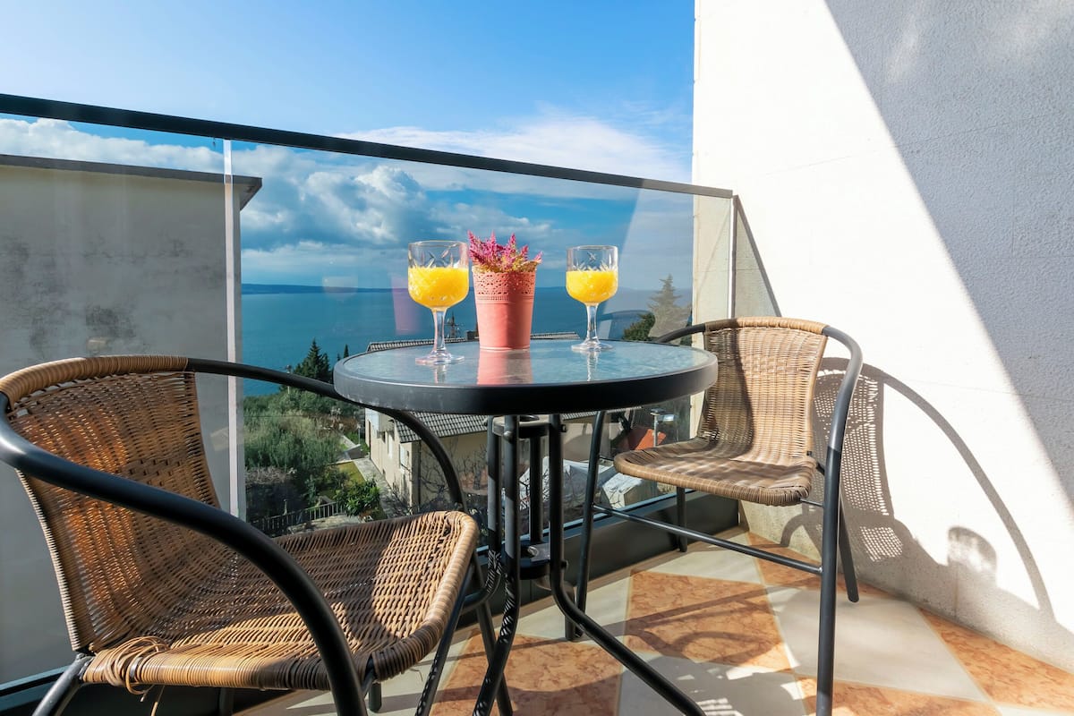 A balcony with wicker chairs, a glass table, and two glasses of orange juice.