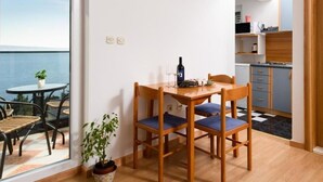A dining area with a wooden table and chairs, a potted plant, and a view of the sea through a large window. - Apartments Villa Milas With Pool (Jesenice)