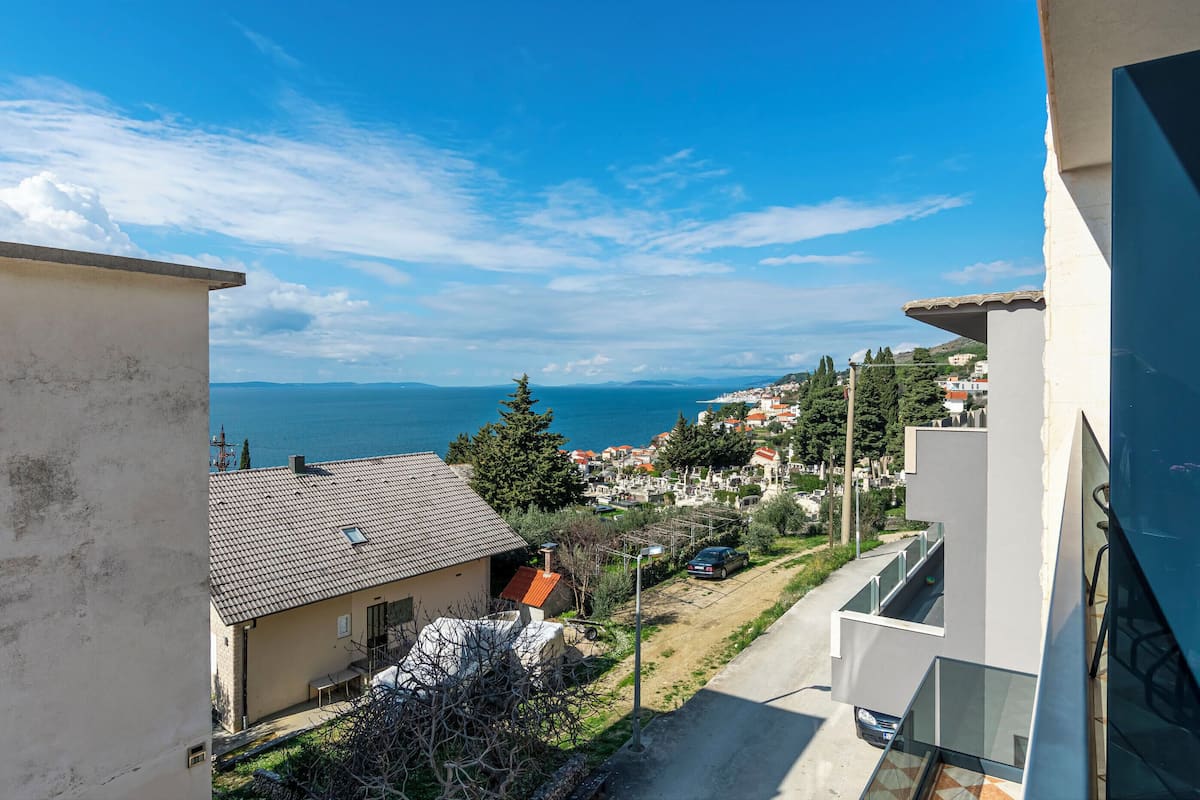 A residential area with a view of the sea, houses with red roofs, and a clear sky.