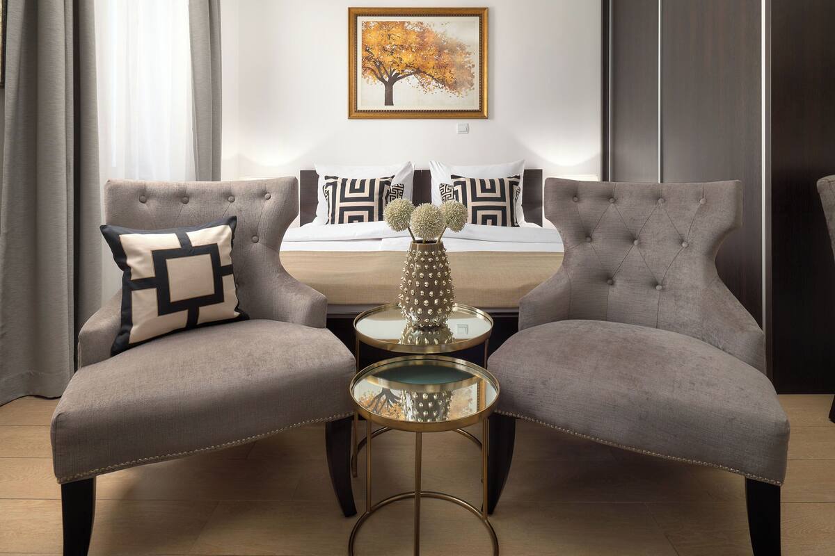 Um quarto com duas poltronas estofadas, uma mesa redonda pequena com tampo de vidro e um vaso decorativo.