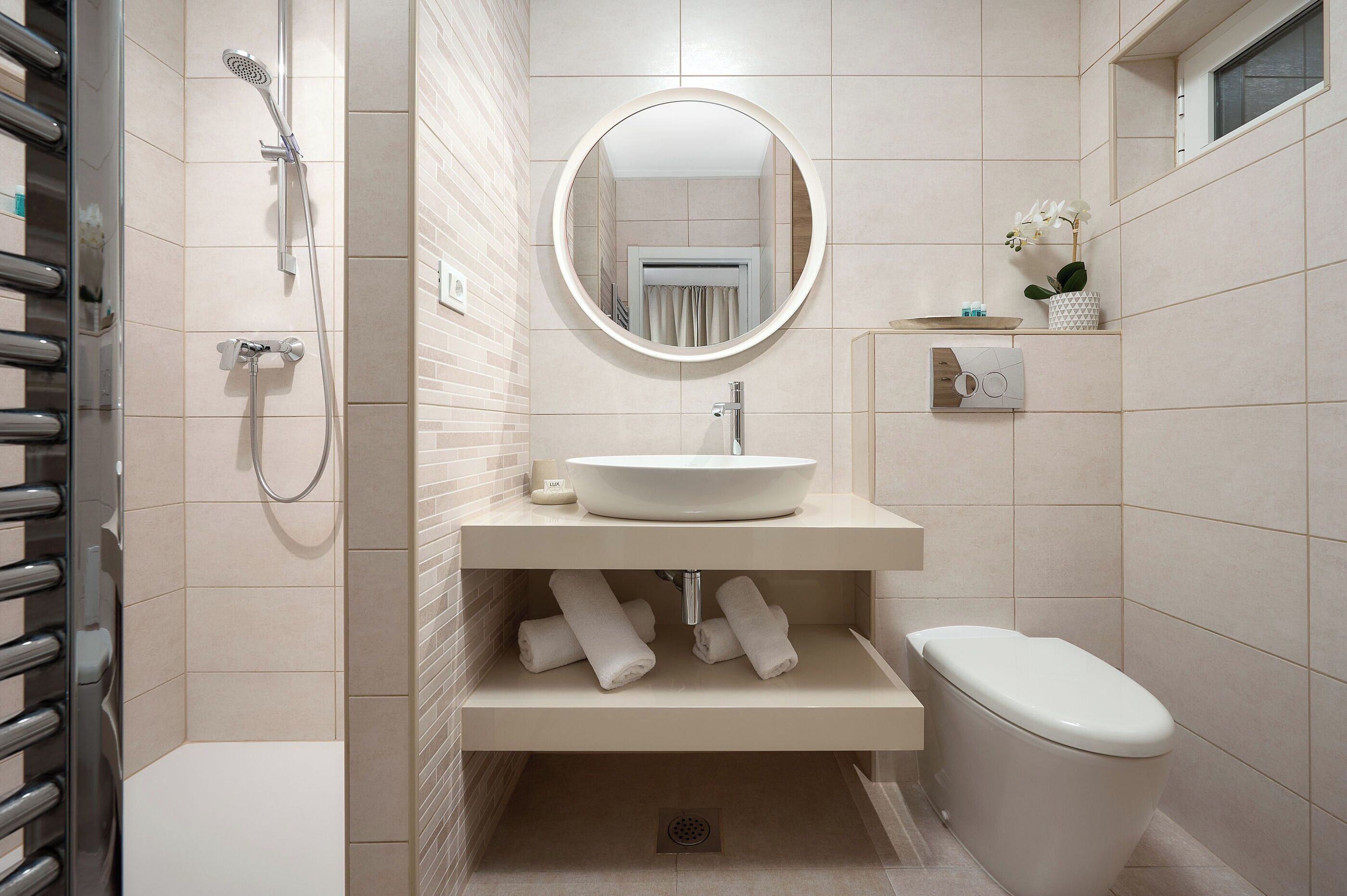 Un baño moderno con un espejo redondo, un lavamanos y un inodoro.