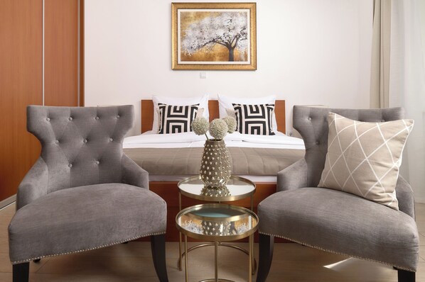 A hotel room with a bed, two armchairs, a small round table, and a decorative vase.