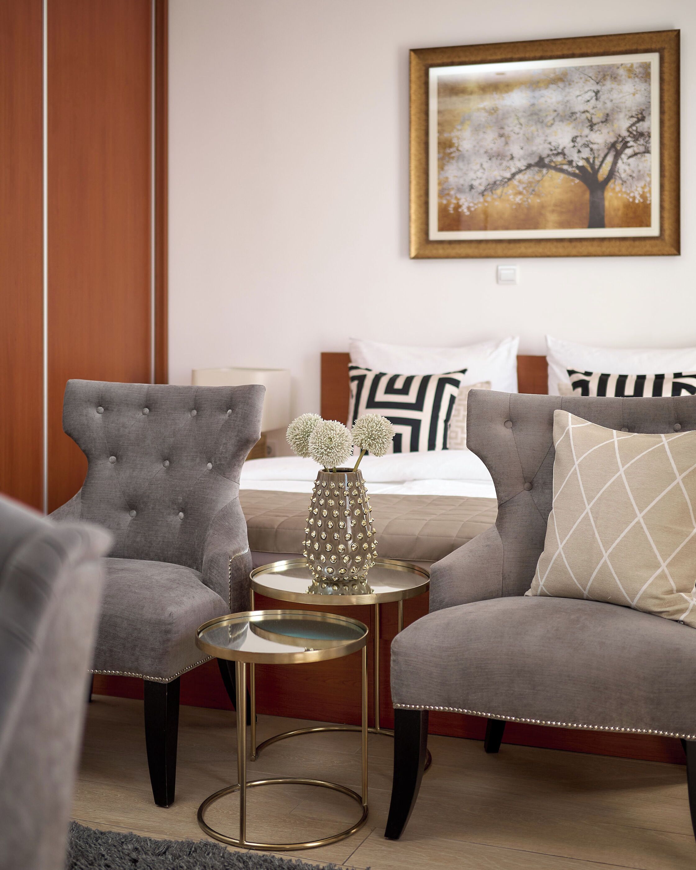 Una habitación de hotel con una cama, dos sillones, una mesita redonda y un jarrón decorativo.
