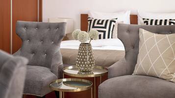 Una habitación de hotel con una cama, dos sillones, una mesita redonda y un jarrón decorativo.