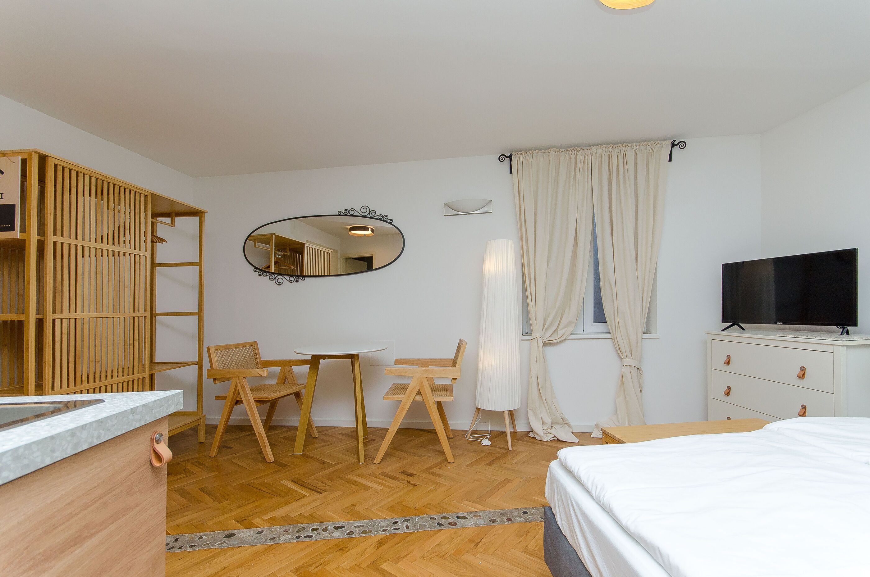 Quarto de hotel com guarda-roupa de madeira, uma escrivaninha com cadeiras, televisão e uma cama.