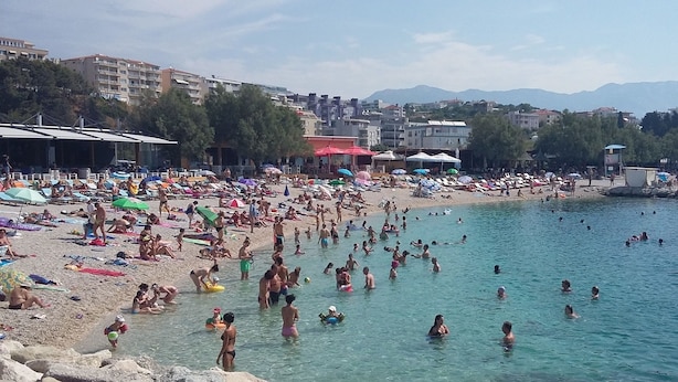 Una playa concurrida, gente tomando el sol y nadando.