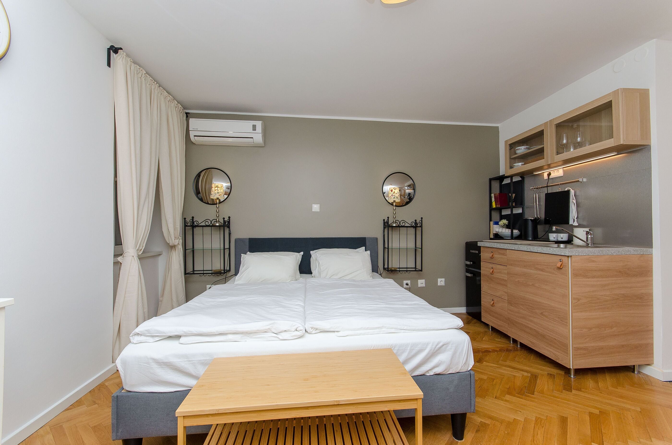Un dormitorio con cama, mesitas de noche, un escritorio de madera, un armario y una kitchenette.