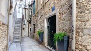 Un estrecho edificio de piedra con una escalera que lleva a una puerta, una reja negra y plantas en macetas en la planta baja.
