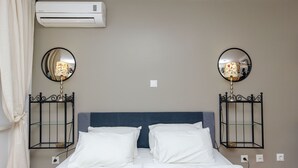 Habitación de hotel con una cama, dos mesitas de noche con lámparas, aire acondicionado y un espejo en la pared.