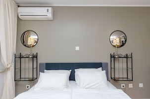 A hotel room with a bed, two bedside tables with lamps, an air conditioner, and a mirror on the wall.