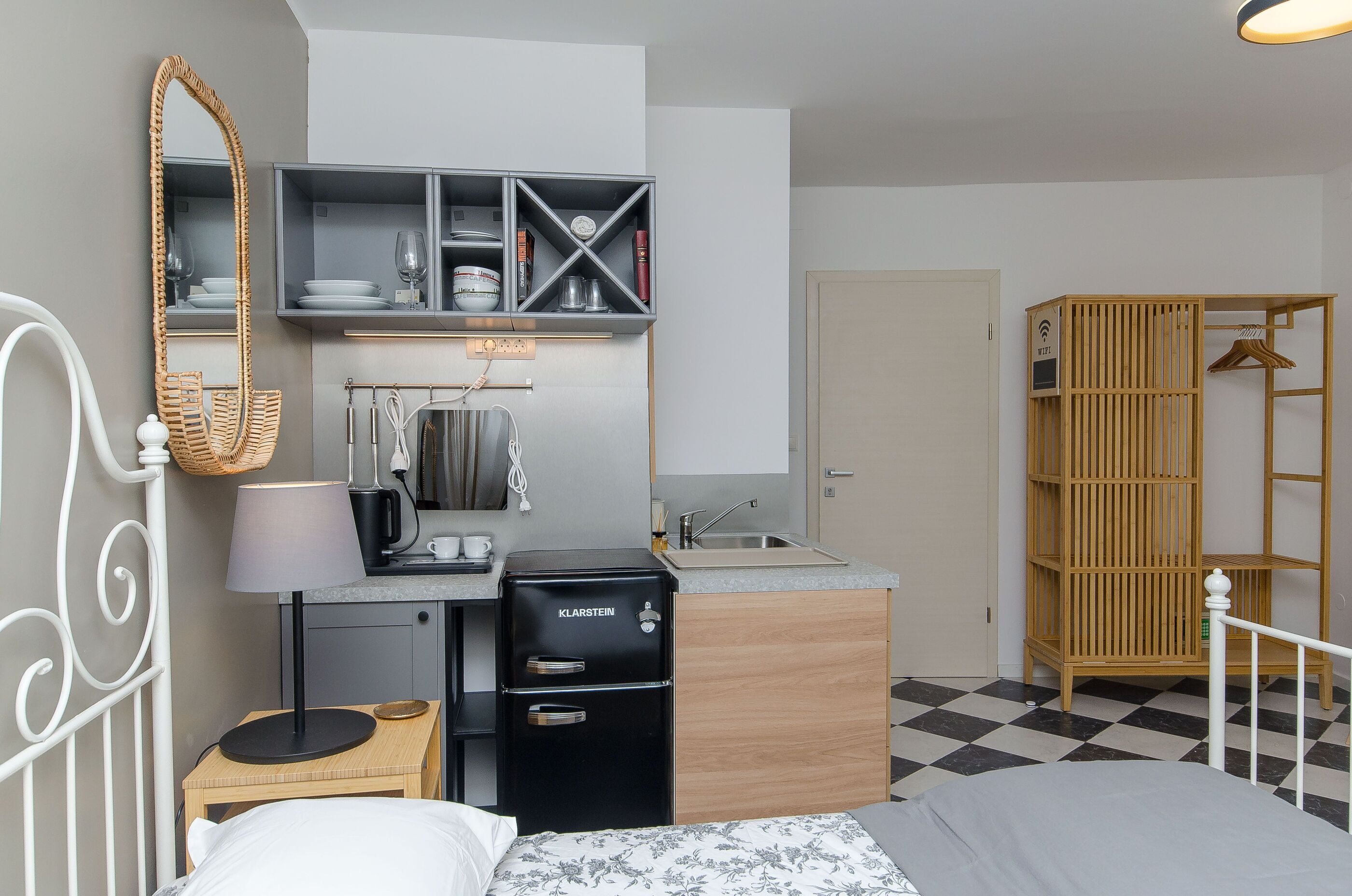 Habitació d'hotel senzilla amb petita cuina, llit, armari i mirall.