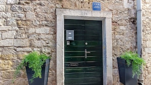 Un edificio de piedra con una puerta verde, dos macetas negras con plantas verdes y un letrero sobre la puerta.