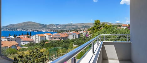 A balcony with a view of a coastal town, a mountain, and a clear blue sky.