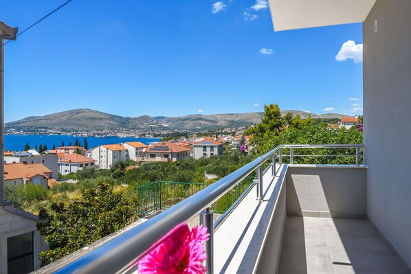 A balcony with a view of a coastal town, a mountain, and a clear blue sky. - Apartments Neli (Okrug Gornji)