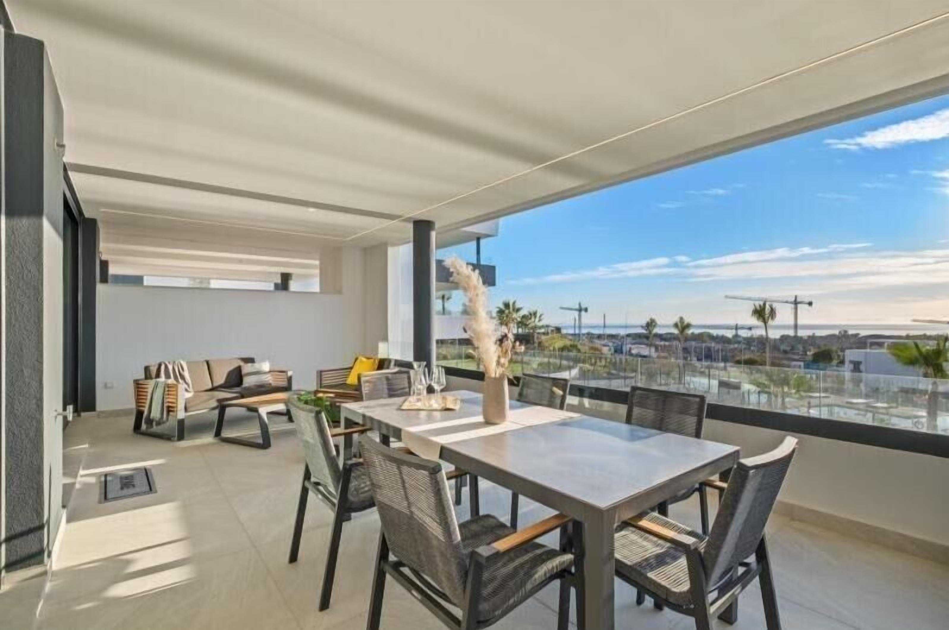 A modern dining area with a large table and chairs, a sofa, and a view of the cityscape through large windows.