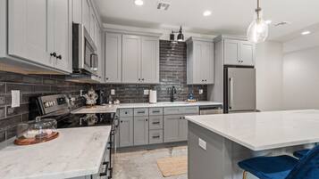 A modern kitchen with grey cabinets, a black tiled backsplash, stainless steel appliances, and a marble countertop.