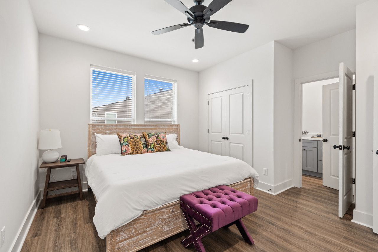 A bedroom with a bed, a nightstand, a ceiling fan, a window, and a door leading to a bathroom.