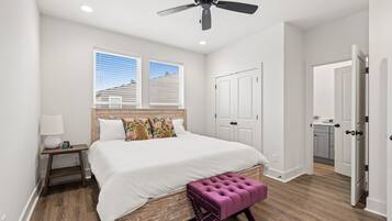 A bedroom with a bed, a nightstand, a ceiling fan, a window, and a door leading to a bathroom.