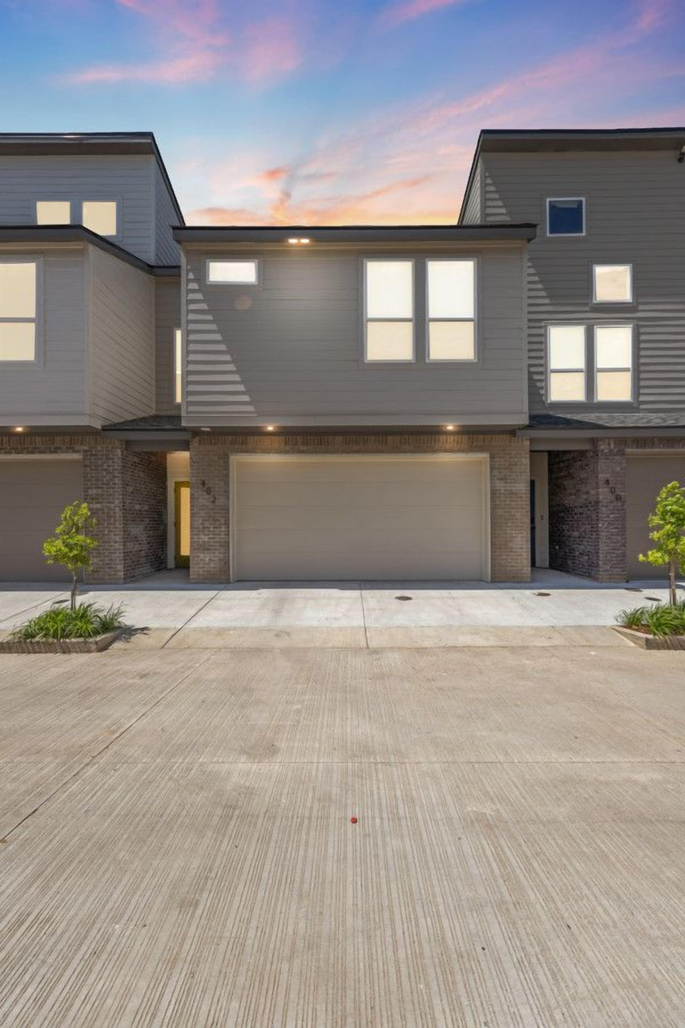 A modern two-story residential building with a garage, a driveway, and small trees in front.