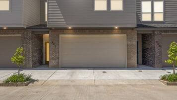 A modern two-story residential building with a garage, a driveway, and small trees in front.
