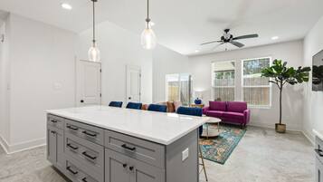 A modern kitchen with a central island, grey cabinets, pendant lighting, and a ceiling fan.