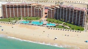 Un hôtel à étages, doté d’un espace piscine central et d’une plage avec des parasols et des chaises longues.