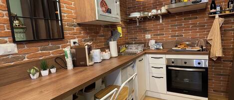 Een keuken met een bakstenen muur, een houten aanrecht, witte kastjes, een magnetron, een oven en barstoelen.