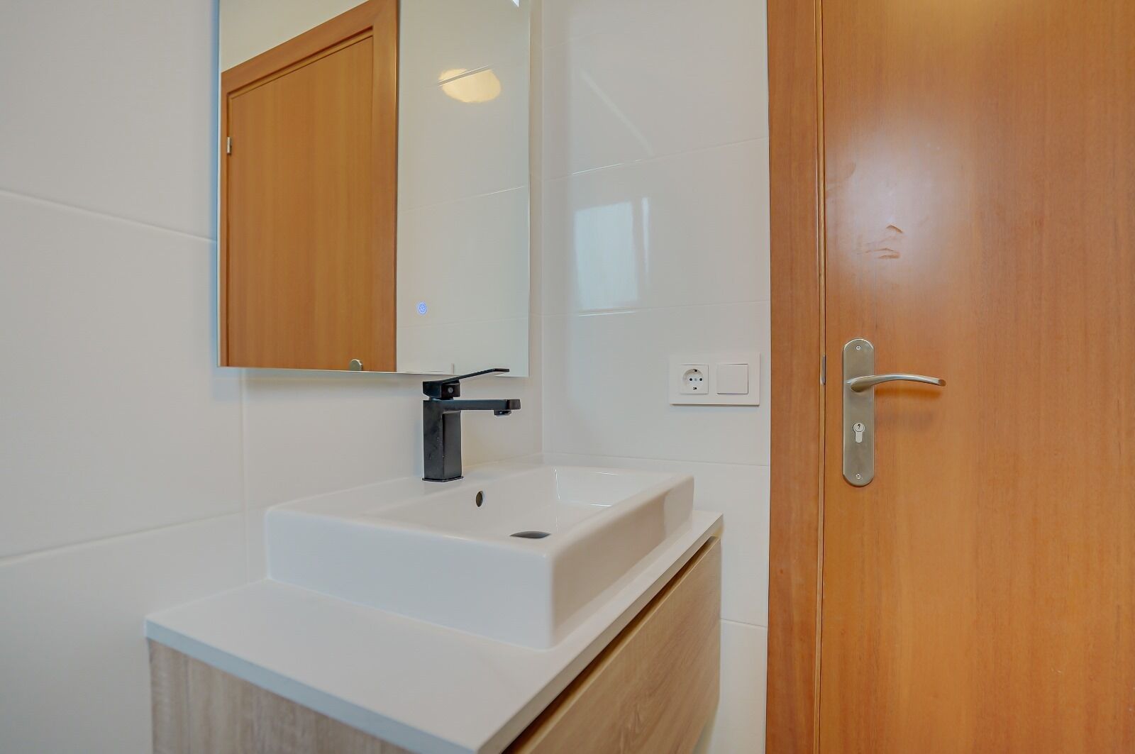 A bathroom with a white sink, a mirror, and a wooden door.
