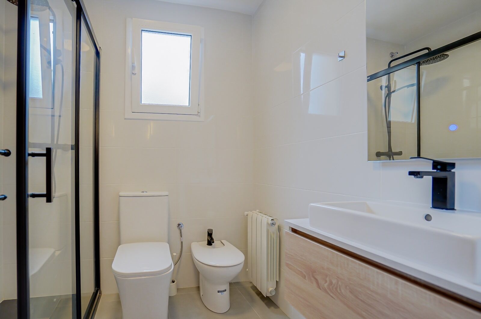 A modern bathroom with a glass shower enclosure, a toilet, a bidet, and a bathtub.