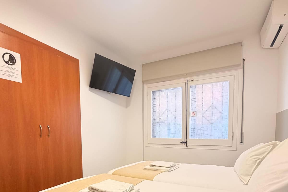 Een slaapkamer met een bed, een houten garderobe, een televisie en een raam met zonwering.