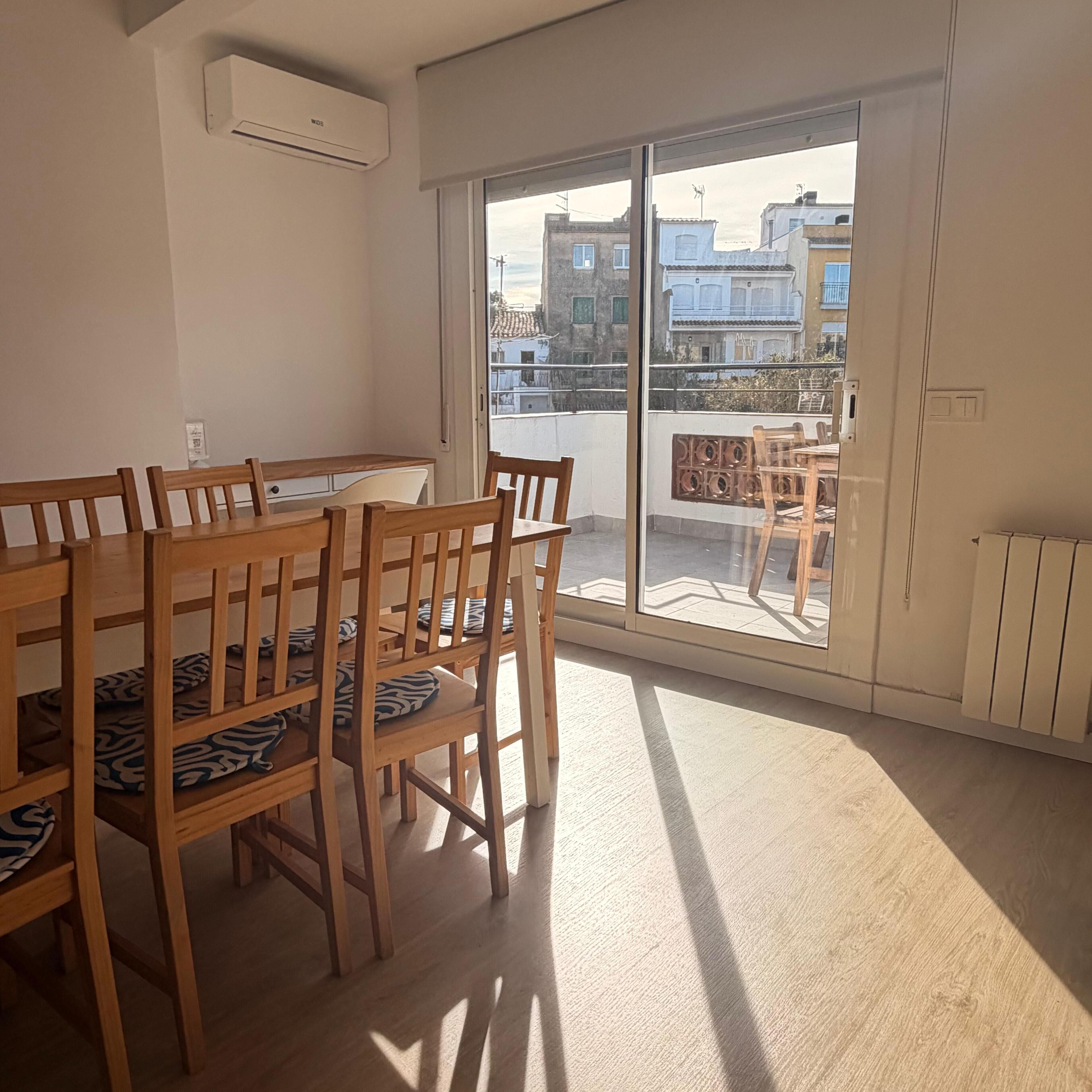 A dining area with a wooden table and chairs, a large sliding glass door leading to an outdoor balcony, and a white air conditioning unit on the wall.