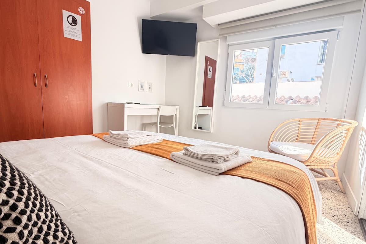 Een hotelkamer met een bed, een bureau, een stoel, een televisie en een raam.