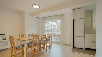 Un comedor con una mesa y sillas de madera, una cocina con refrigerador y vistas a edificios a través de un ventanal grande.