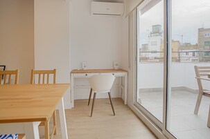 Una habitación moderna con un escritorio de madera, una silla blanca y un ventanal con vistas a la ciudad.