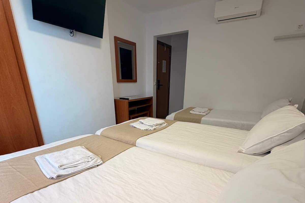Een hotelkamer met twee bedden, een aan de muur bevestigde televisie en een airconditioning.