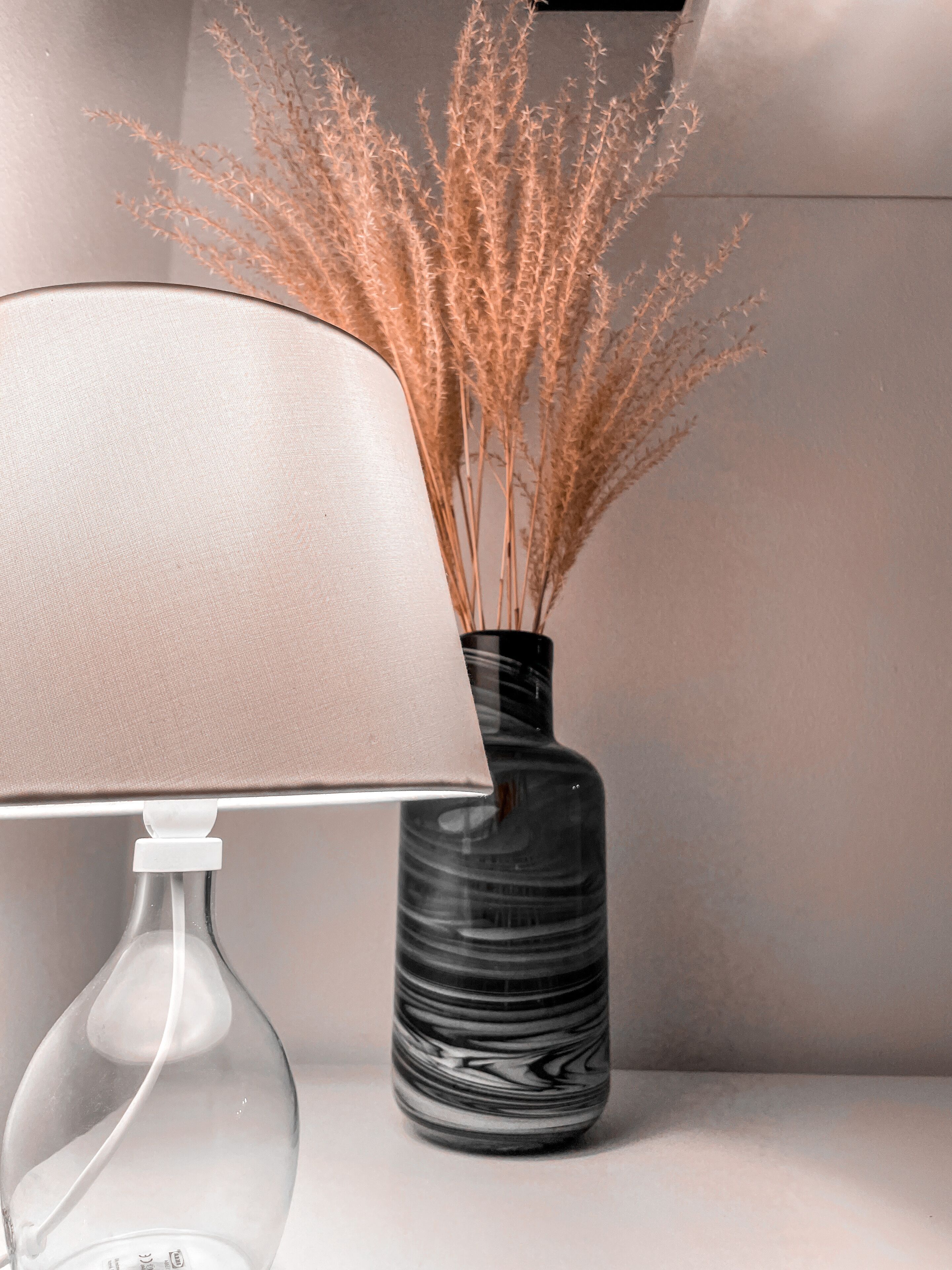 Eine Lampe mit beigeem Lampenschirm und eine Vase mit getrocknetem Pampasgras.