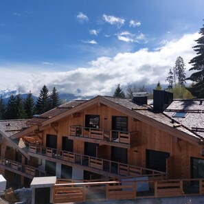 A wooden cabin with a balcony, a small attached structure, and a view of mountains in the background. - Luxury apartment 6-8 pers. with Balcony - small garden foot of slopes Combloux (Combloux)