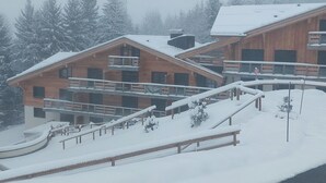 A snow-covered wooden building with multiple balconies and a ski lift visible in the background.