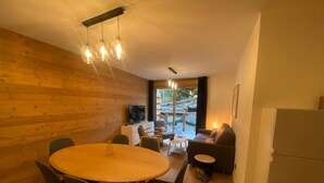 A cozy room with a wooden wall, a round dining table with chairs, a sofa, and a television.
