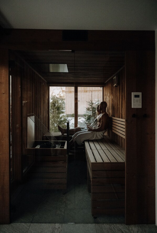 A wooden interior with a bench and a small table, a window with a view of trees, and a wooden door.