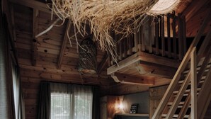Une chambre confortable dans un chalet en bois, avec un lit, une chaise, un escalier et une suspension lumineuse.