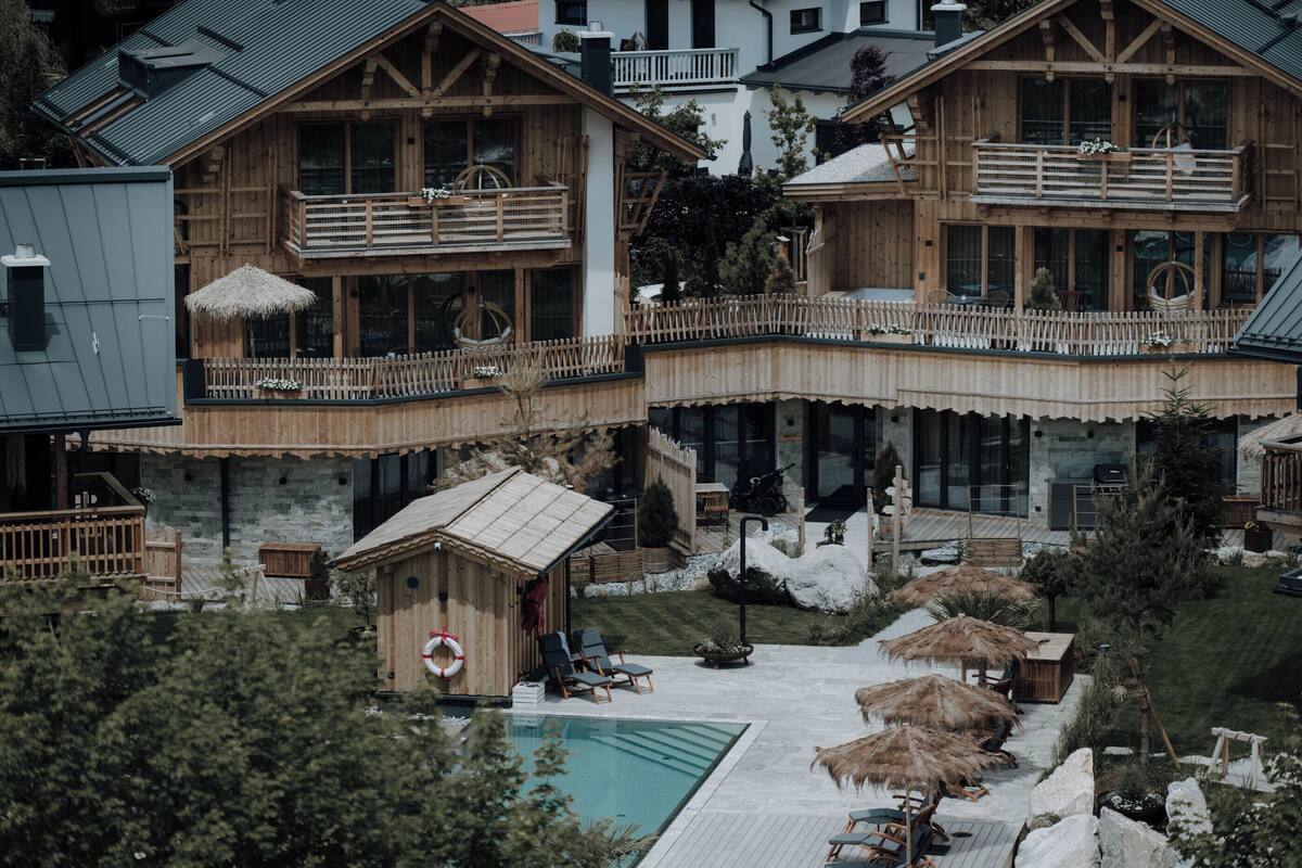 Una cabaña de madera con piscina, sillones de descanso y sombrillas.