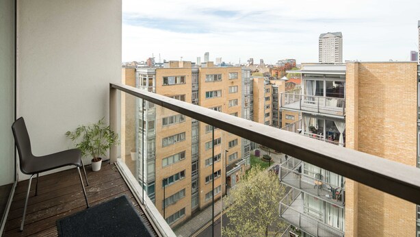 Un balcon donnant sur un paysage urbain, une plante en pot et une chaise.