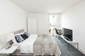 A modern hotel room with a bed, a desk, a TV, and a large window.