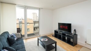 Un salon moderne comprenant un canapé, une table basse, un téléviseur et une porte-fenêtre coulissante donnant sur un balcon.