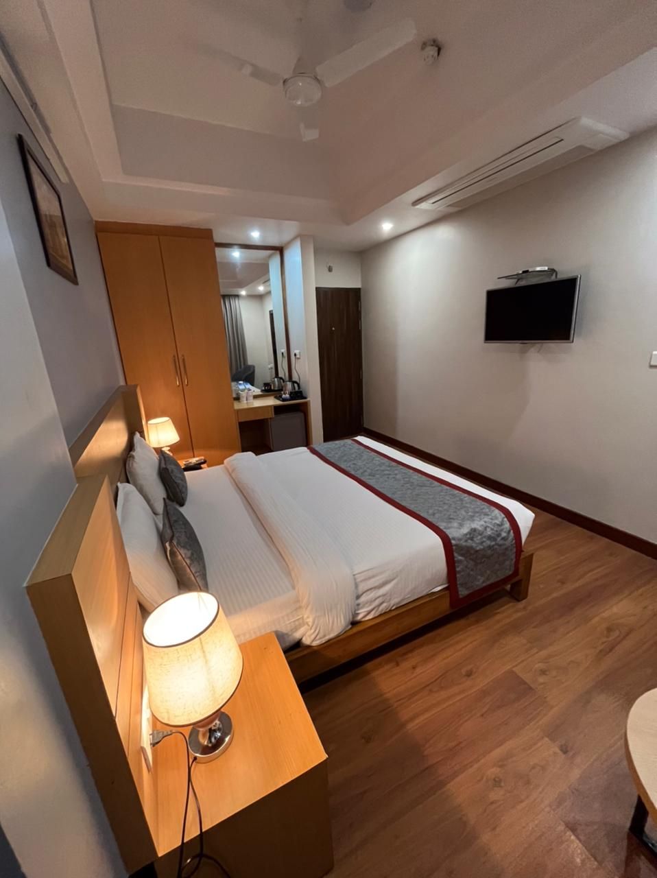 A bedroom with a bed, bedside table, lamp, wardrobe, and a mounted TV.