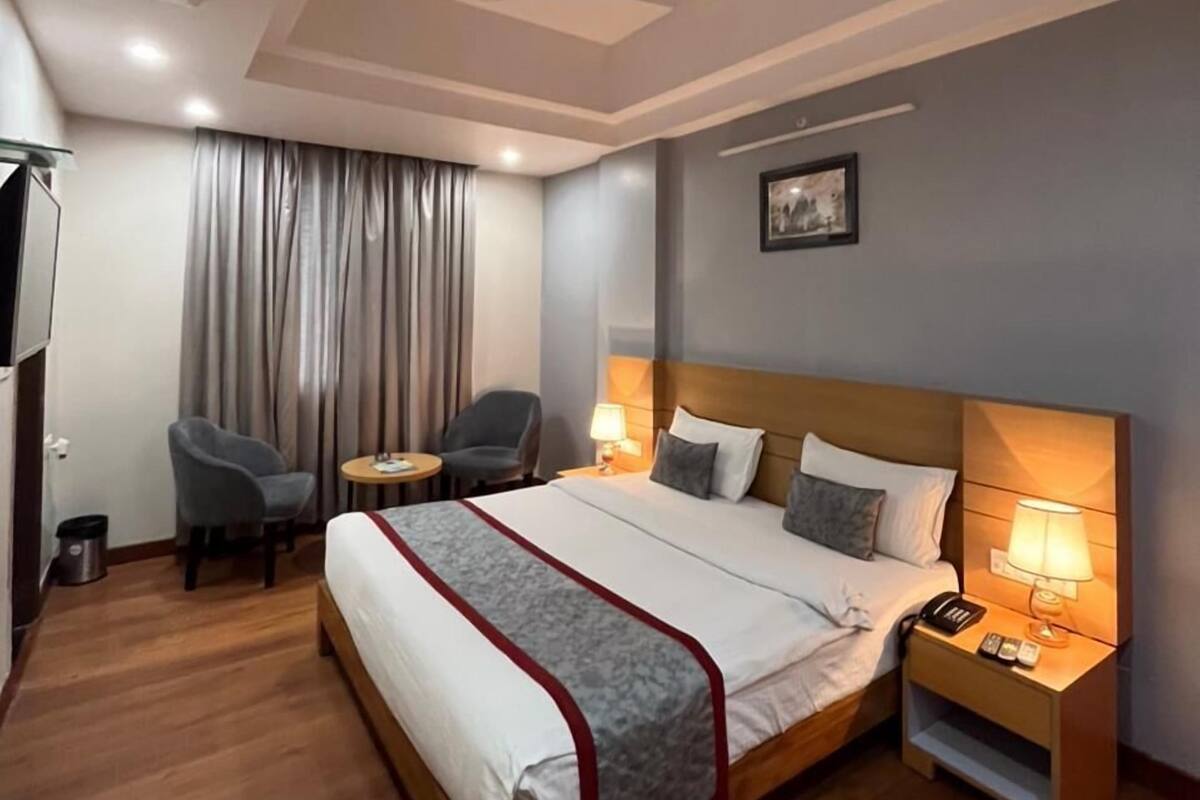 A hotel room with a large bed, two bedside tables, a ceiling fan, a desk with a chair, and a window with curtains.