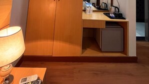 A hotel room with a wooden wardrobe, a bedside table with a lamp, and a small desk with a kettle and cups. - Hotel Sarvin (Lucknow)