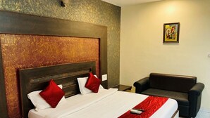 Habitación de hotel con una cama grande, cabecera de madera, manta roja, sofá de cuero negro y un cuadro en la pared.